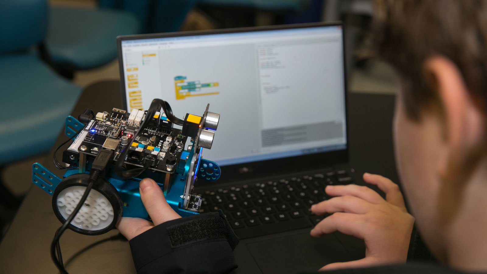 A student programs a LEGO robot using a diagram displayed on a computer screen.