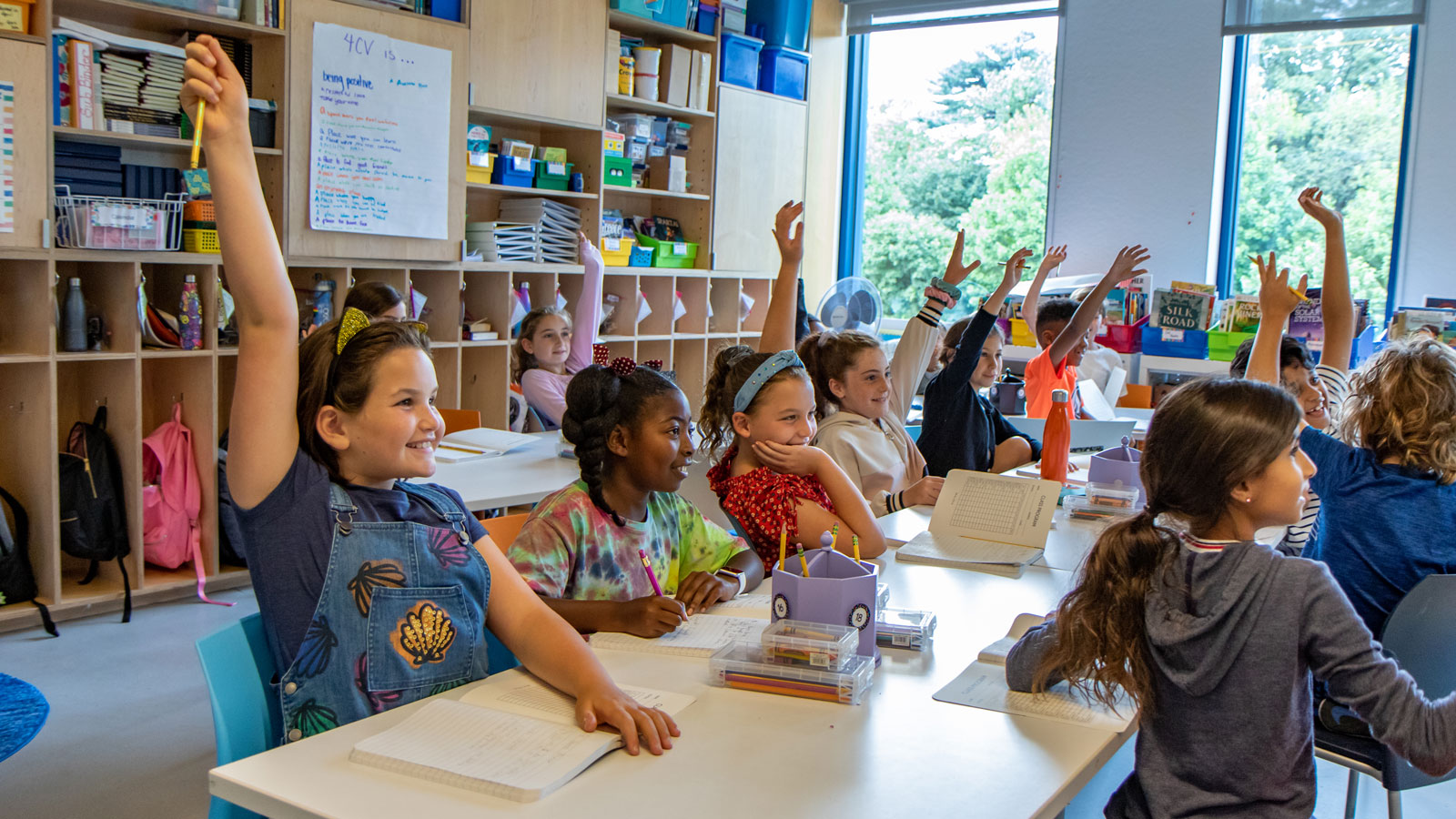 Third grade students raise their hands in class.