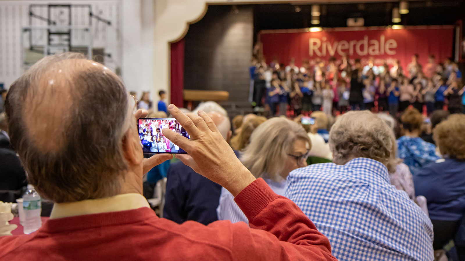 Grandparents watch children sing on the stage of the Lower School gym.