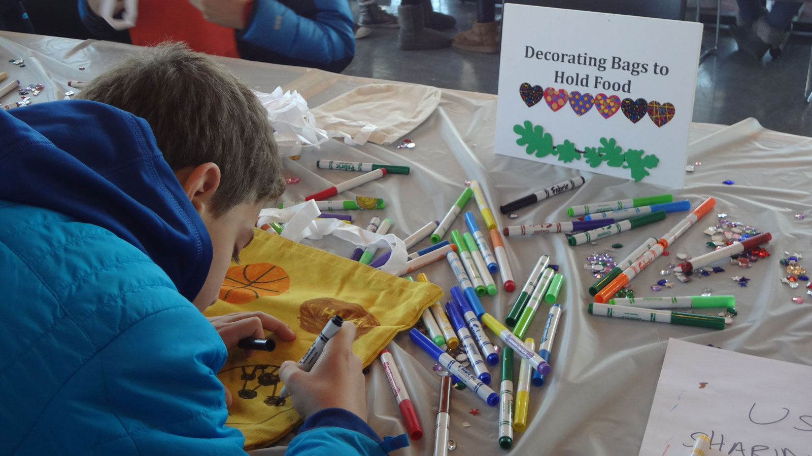 A child draws on a canvas bag to hold food donations.