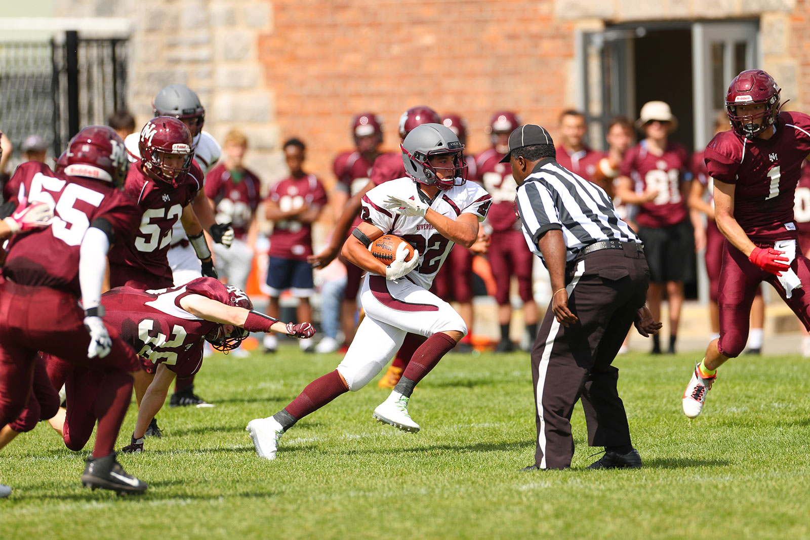A Riverdale football play runs down the fall with the ball as a referee watches.