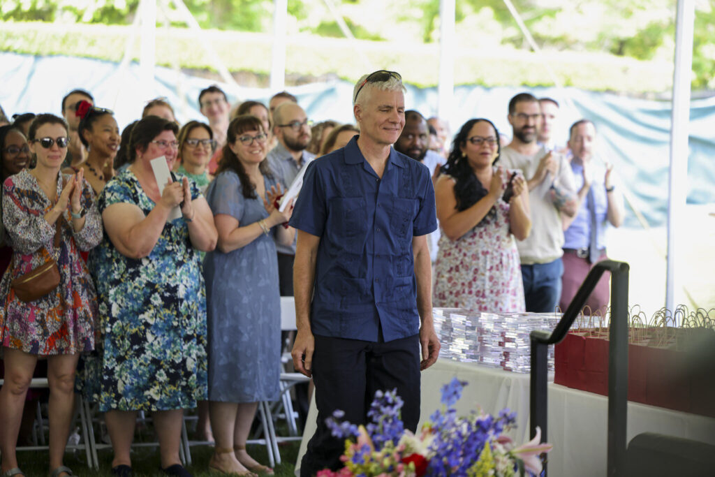 A person stands while others clap in the background.
