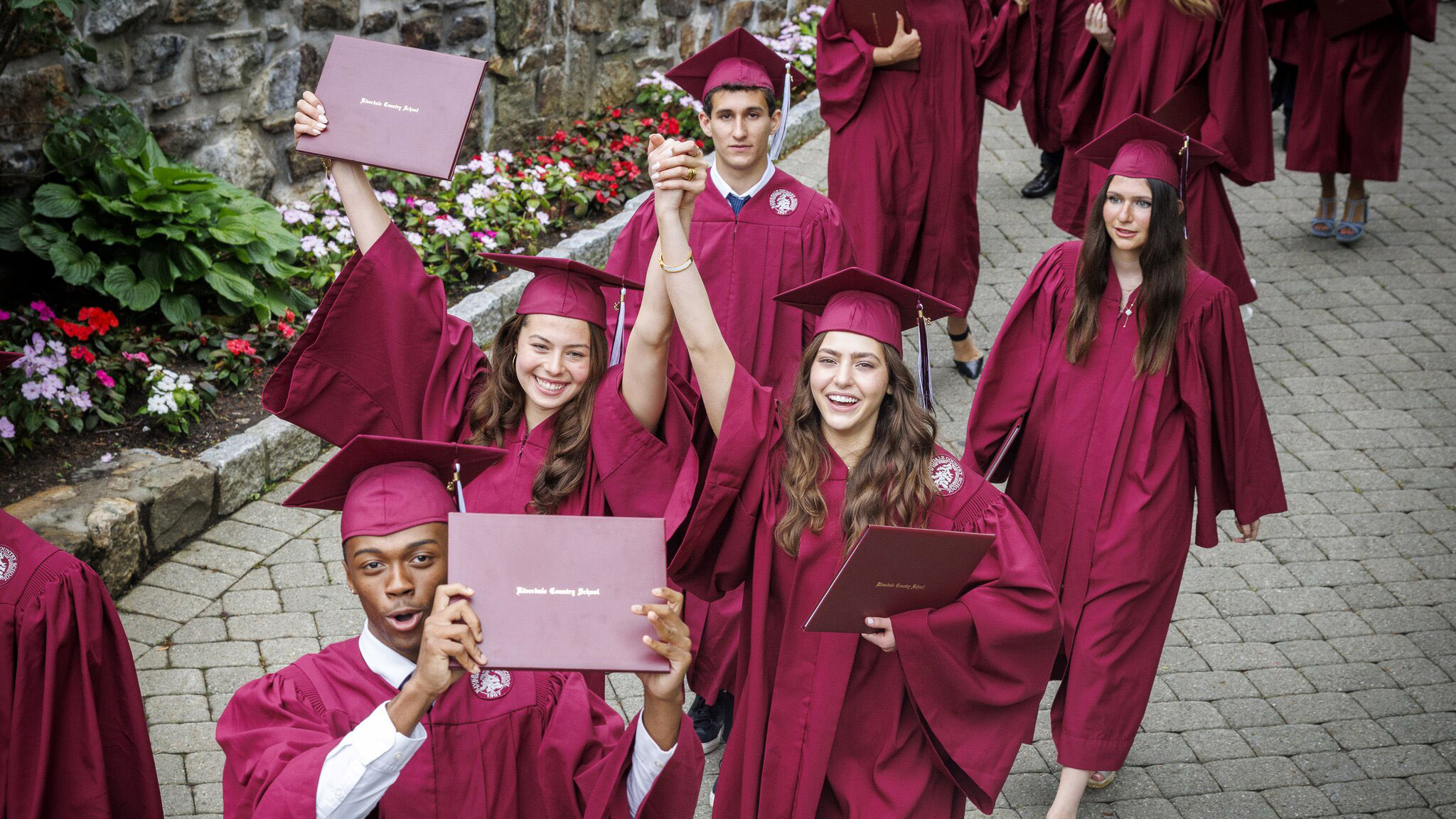 A group of students in caps and gowns hold up diplomas and smile